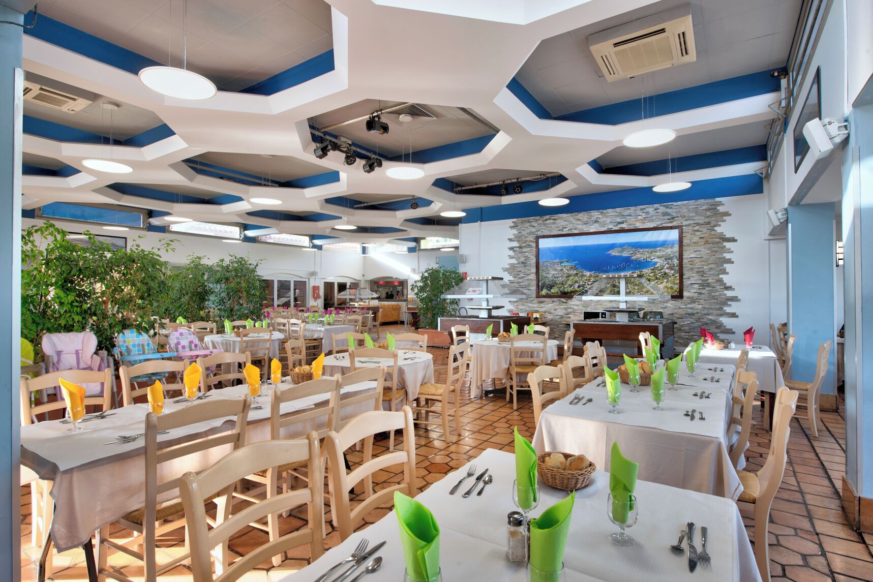 Un restaurant doté de nombreuses tables, de chaises et d’un grand écran de télévision diffusant un paysage pittoresque.