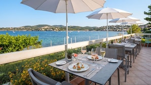 An outdoor dining area with tables, chairs, and umbrellas overlooking a body of water with boats. - Village Club Les Mas de L'Esterel (Saint-Raphael)