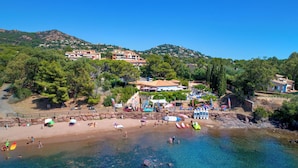 A coastal beach with clear water, beach umbrellas, and a rocky shoreline. - Village Club Les Mas de L'Esterel (Saint-Raphael)