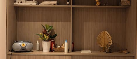 A neatly organized bedroom with a bed, a bedside table, a shelf with toiletries, and a wall-mounted radio.