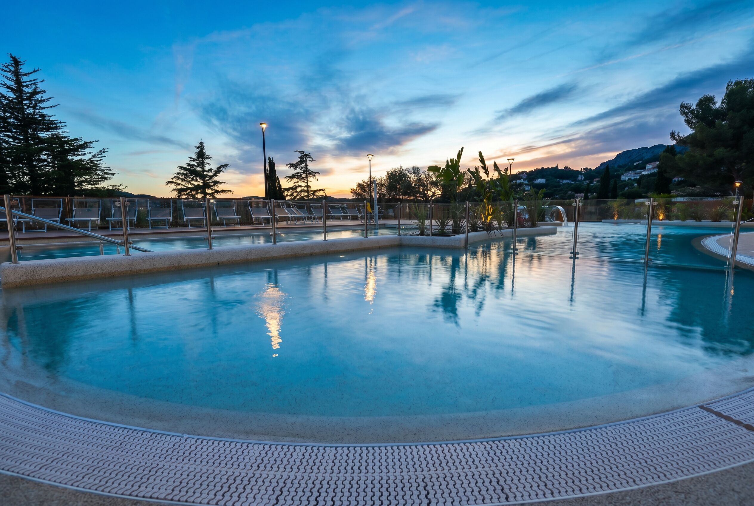 A swimming pool with a tiled deck, metal railings, and a sunset view.
