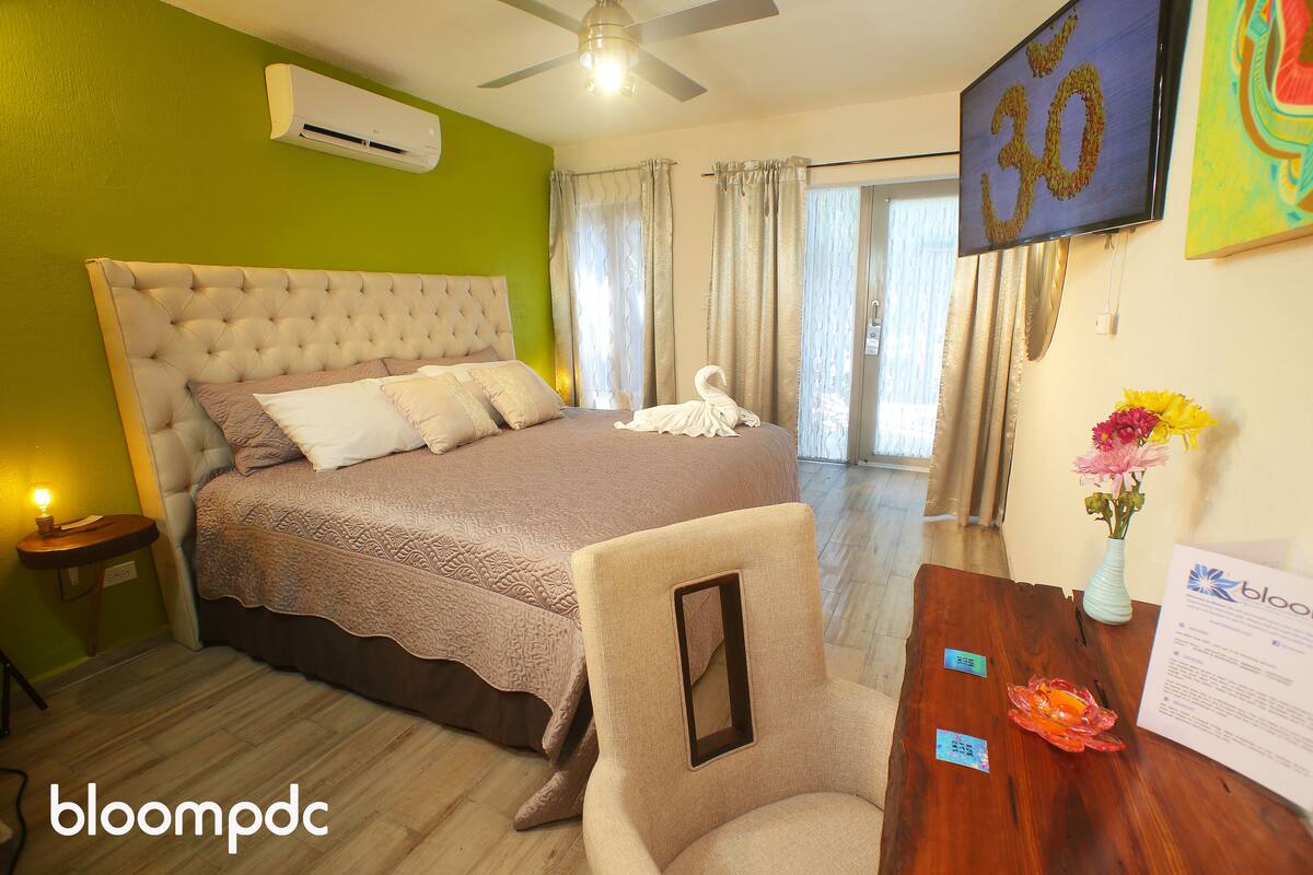 A hotel room with a large bed, a wooden desk, a vase with flowers, and a wall-mounted TV.