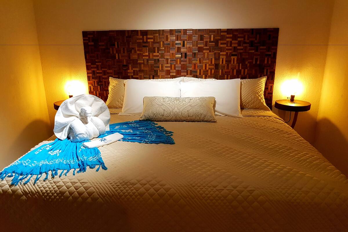 A hotel room with a wooden headboard, a bed with a quilted cover, two bedside lamps, and a blue throw blanket.