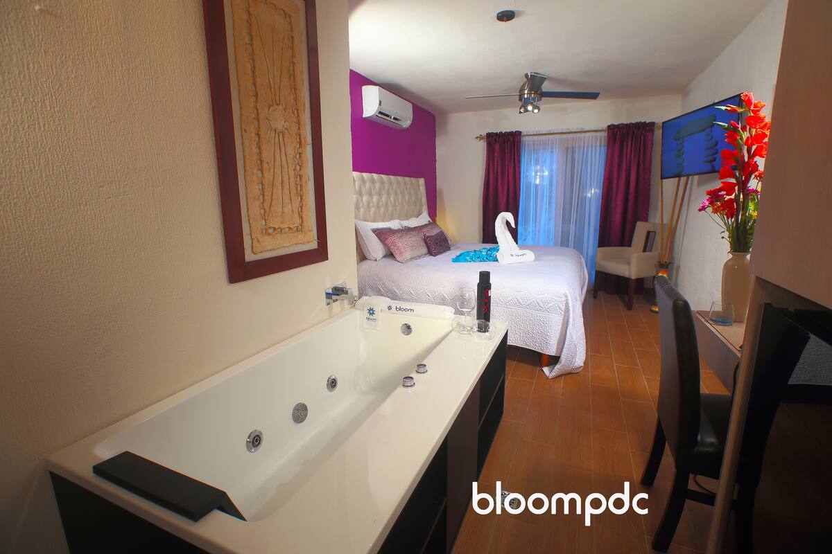 A hotel room with a large bathtub, a bed with a swan-shaped pillow, a desk with a chair, and a television.