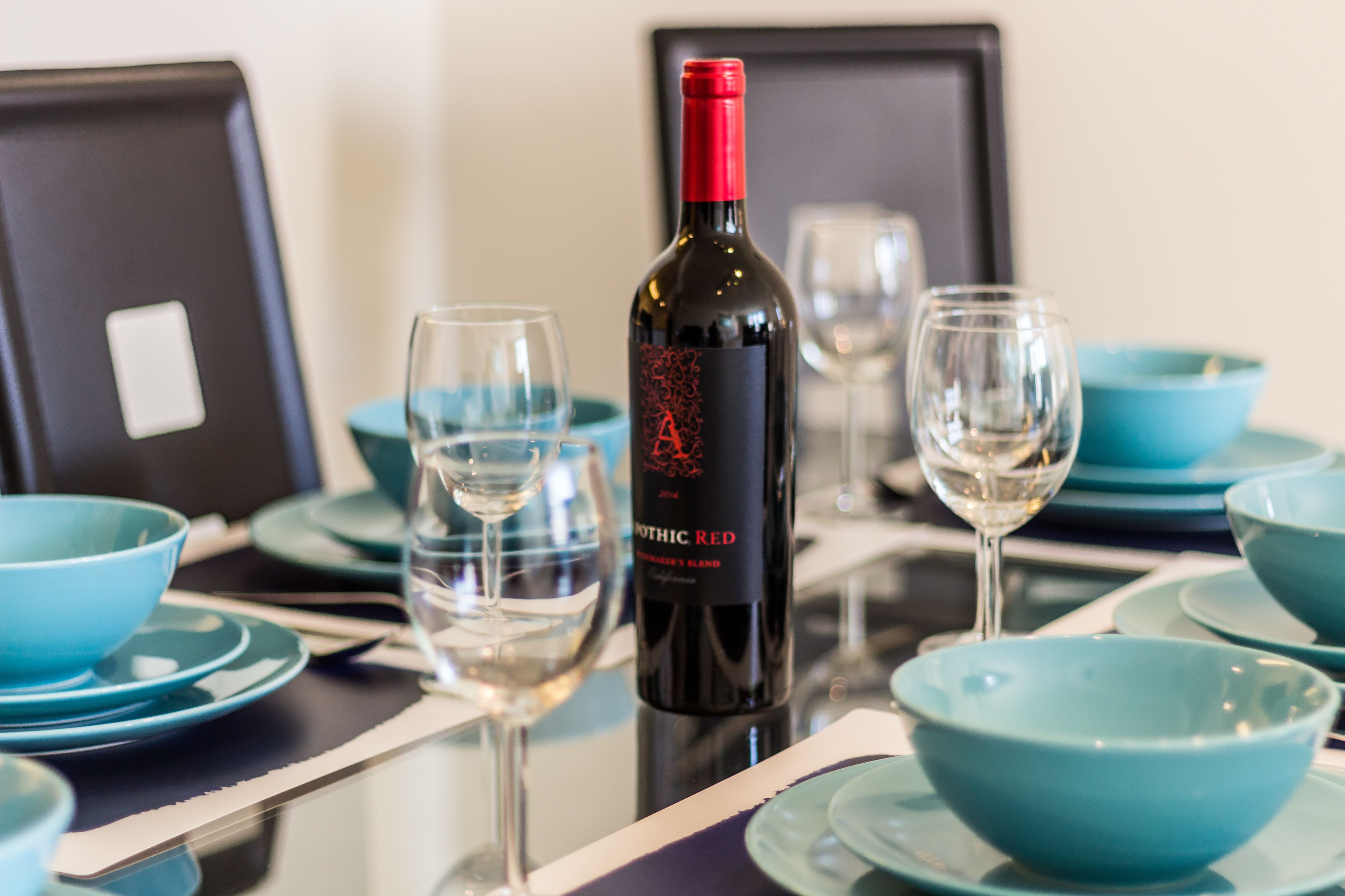 Une table à manger avec une bouteille de vin, des verres et des bols bleus.