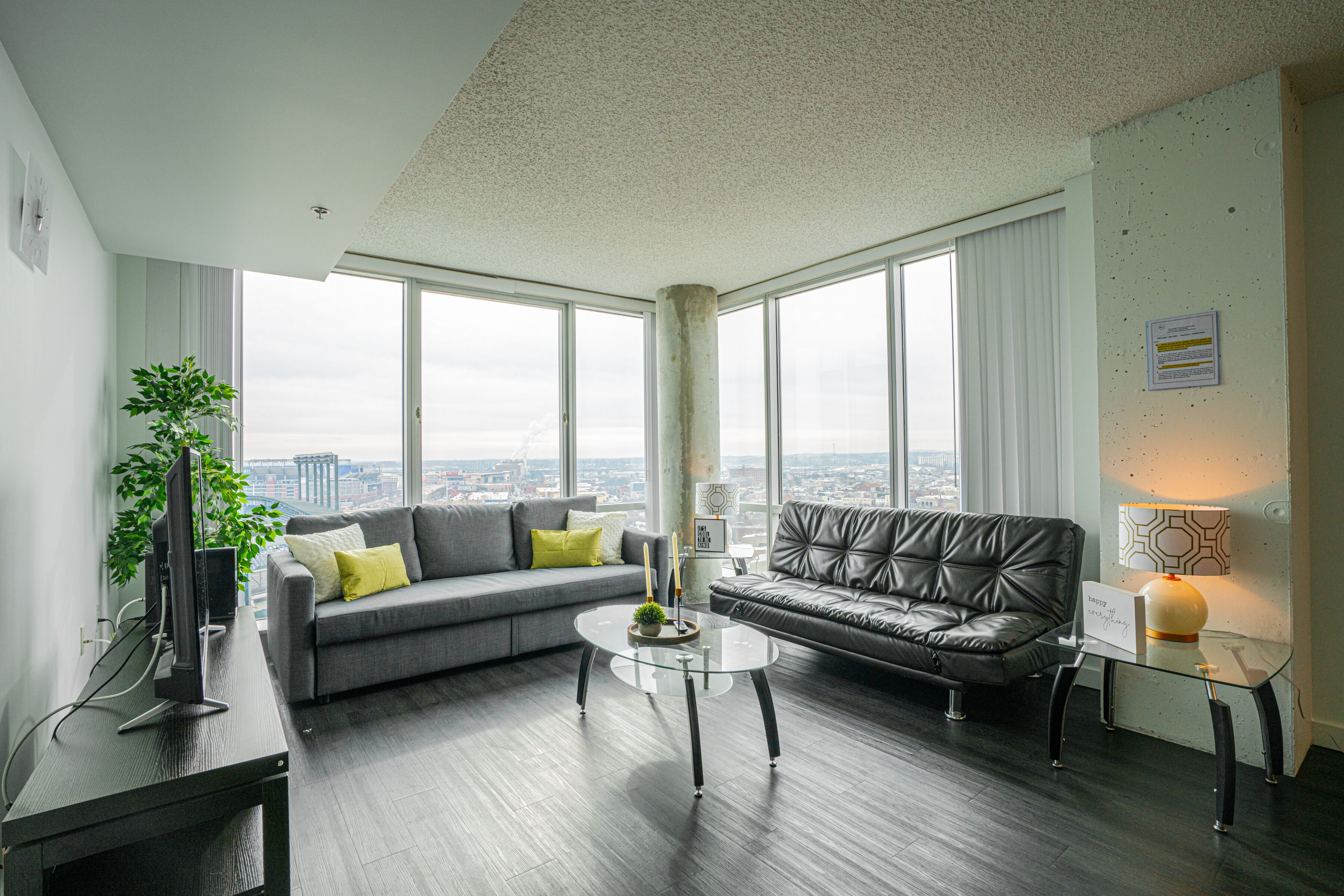 A modern living room with a grey sofa, a glass coffee table, and a leather couch.