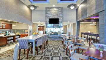 A spacious hotel lobby with a central seating area, a kitchen in the background, and a modern ceiling design.