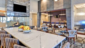 A modern hotel lobby with a marble reception desk, seating area, and a bar. - Homewood Suites by Hilton New Hartford Utica (New Hartford)