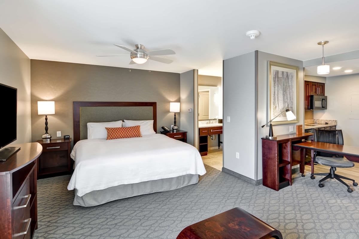 Ein Hotelzimmer mit Bett, Schreibtisch, Stuhl, Fernseher und Deckenventilator.