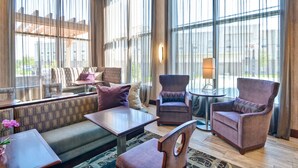 A spacious lobby with a sofa, armchairs, and a small table. Large windows provide natural light and a view of the outside. - Homewood Suites by Hilton New Hartford Utica (New Hartford)