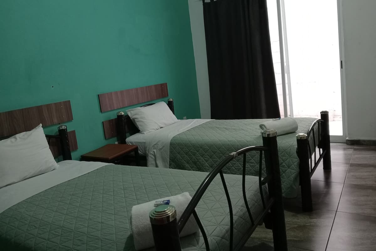 A hotel room with two beds, a window with black curtains, and a view of the outside.