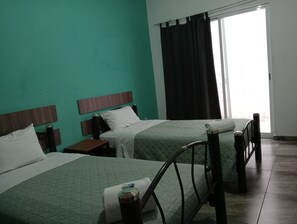 Habitación de hotel con dos camas, una ventana con cortinas oscuras y vistas al exterior.