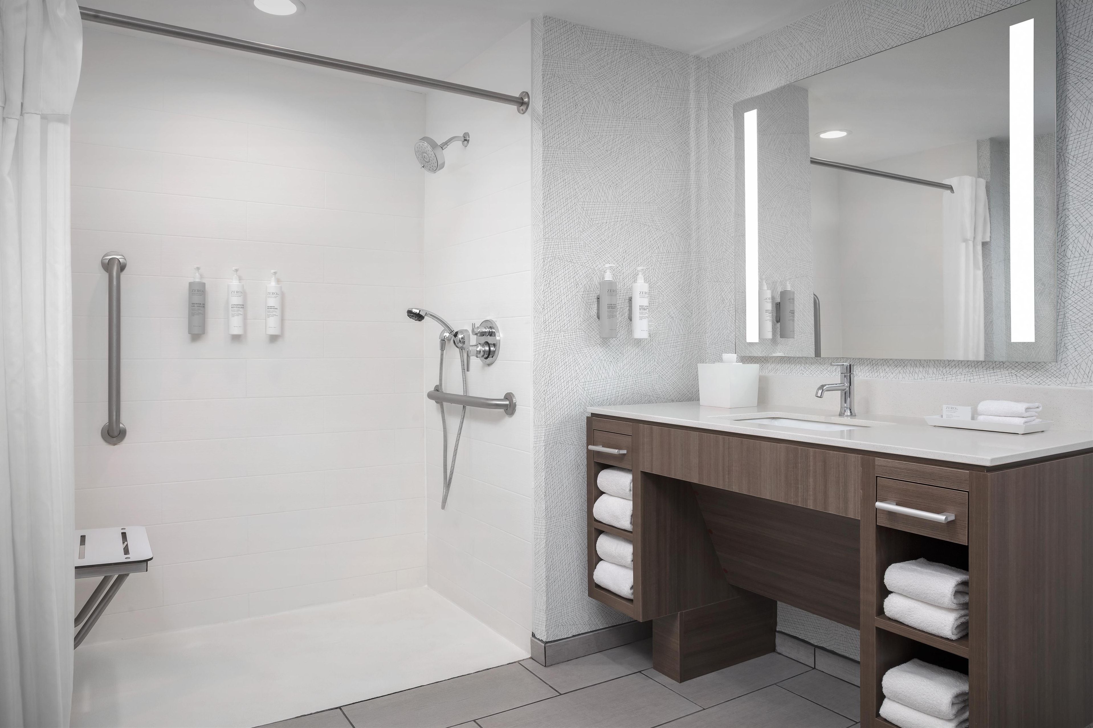 Une salle de bain moderne dotée d’une douche à l’italienne, d’un meuble-lavabo avec miroir et d’un porte-serviettes.