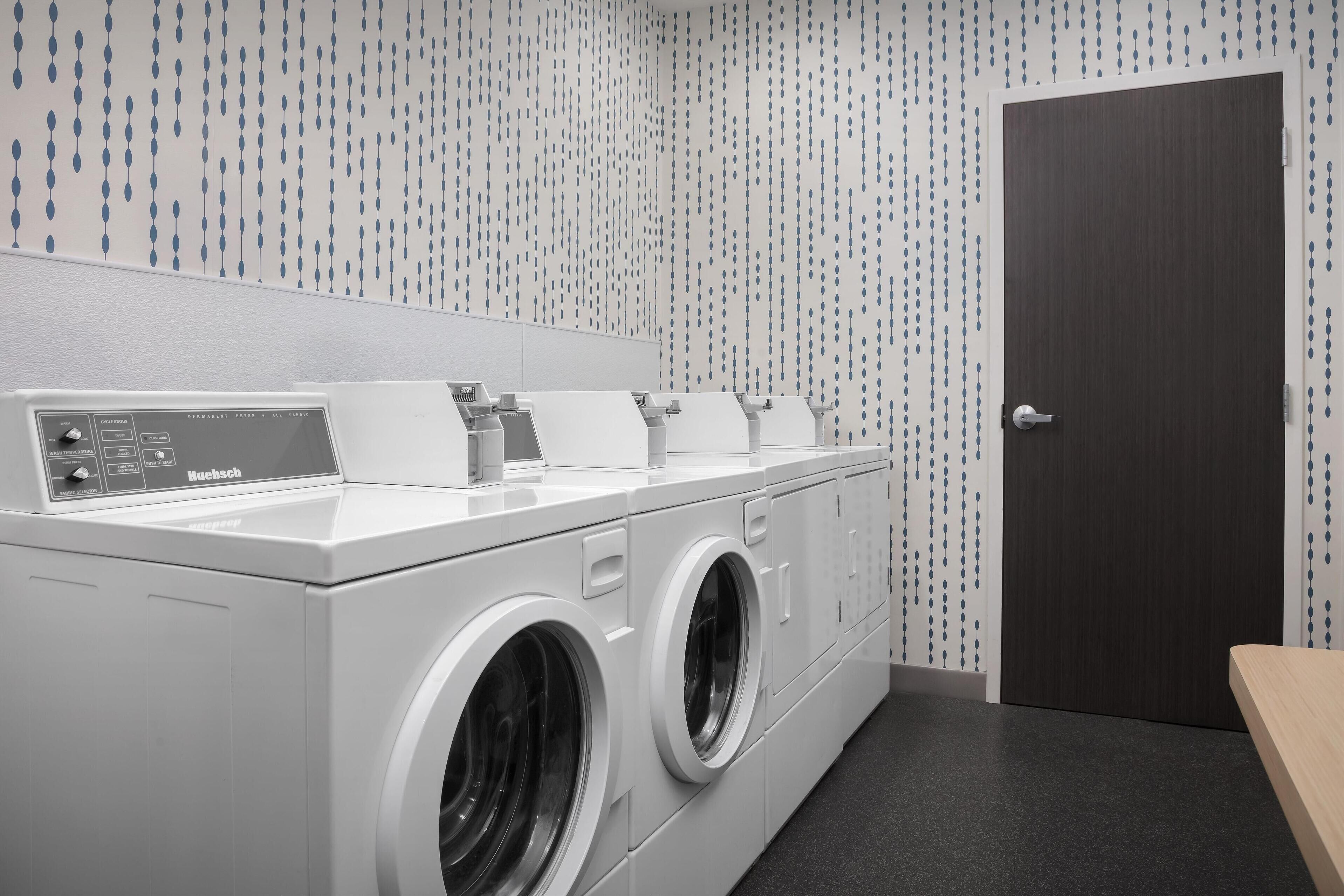 A modern laundry room with a front-loading washing machine and dryer, a control panel, and a door.