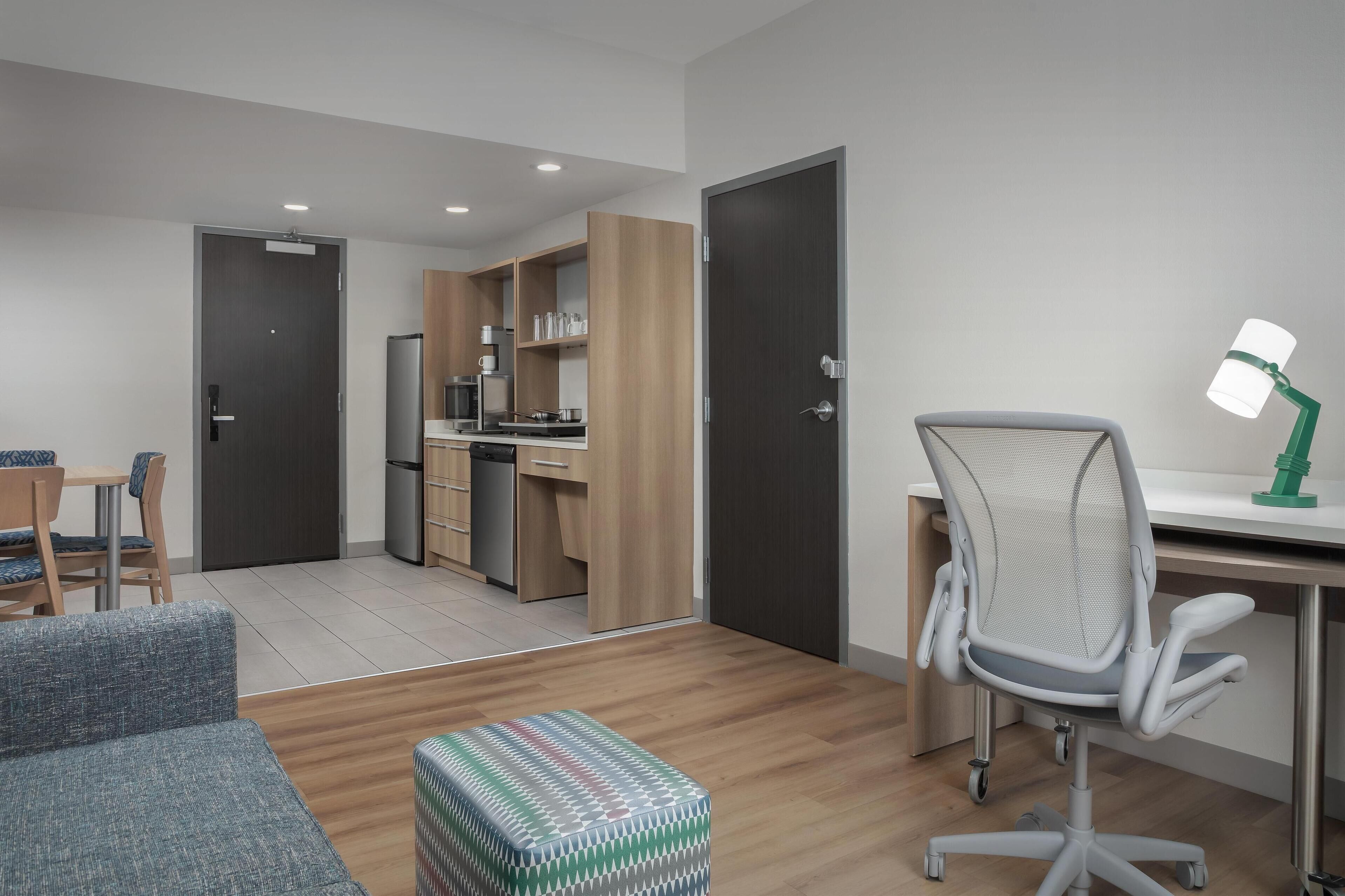 Eine moderne Wohnung mit Küchenzeile, Essbereich, Arbeitsplatz mit Schreibtisch und Stuhl sowie einer kleinen Sitzecke mit Sofa und Hocker.
