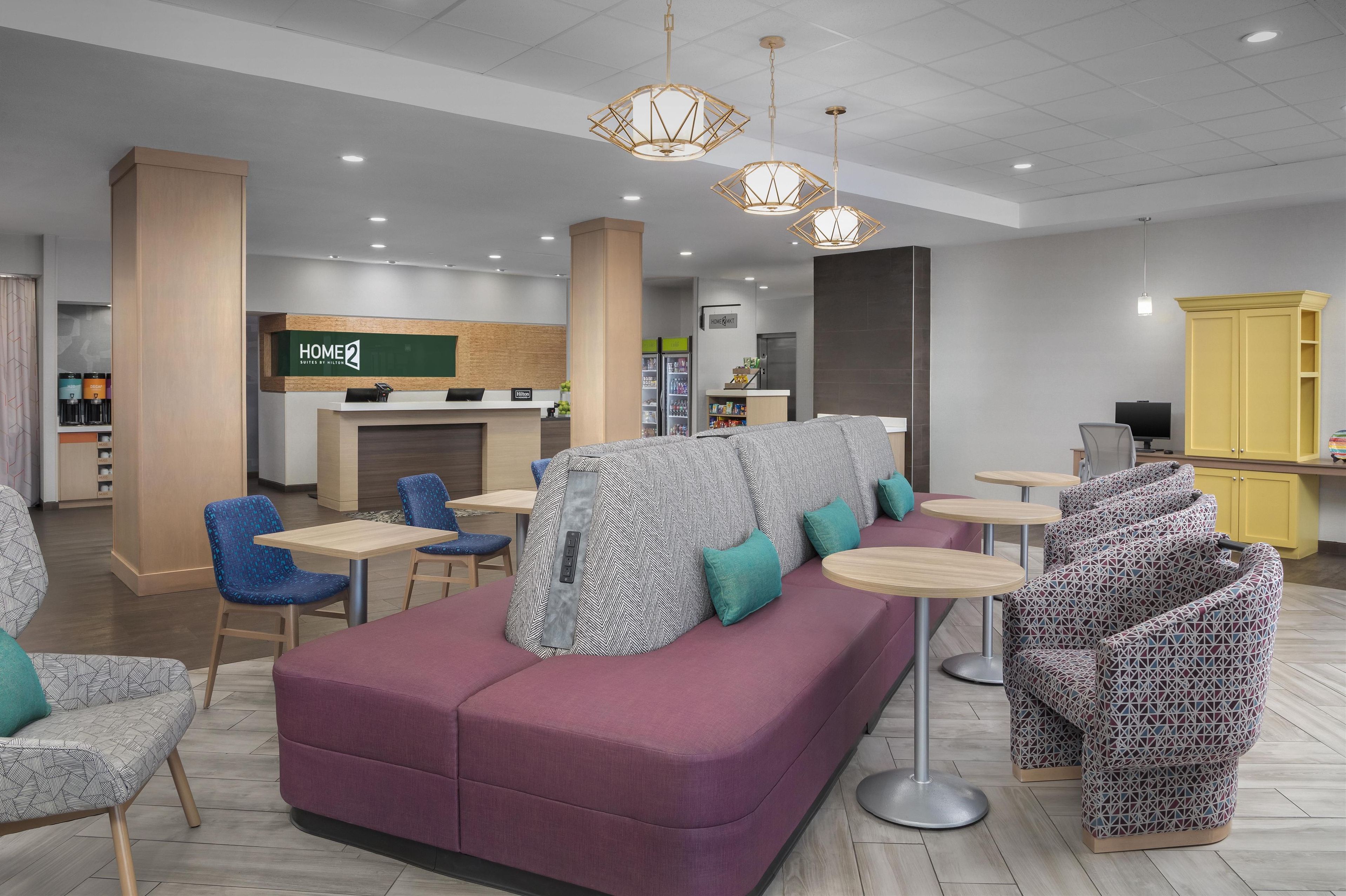 Un área de lounge moderna con una recepción, diferentes disposiciones de asientos y una kitchenette al fondo.