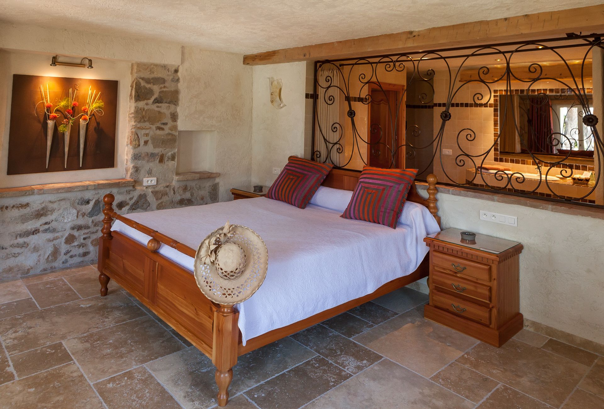 A bedroom with a wooden bed, a nightstand, a mirror, and a stone wall.