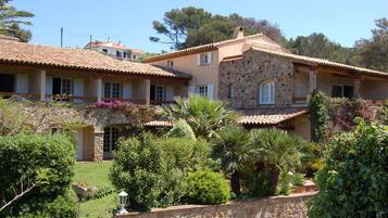 A stone building with a tiled roof, surrounded by lush greenery and a stone wall.