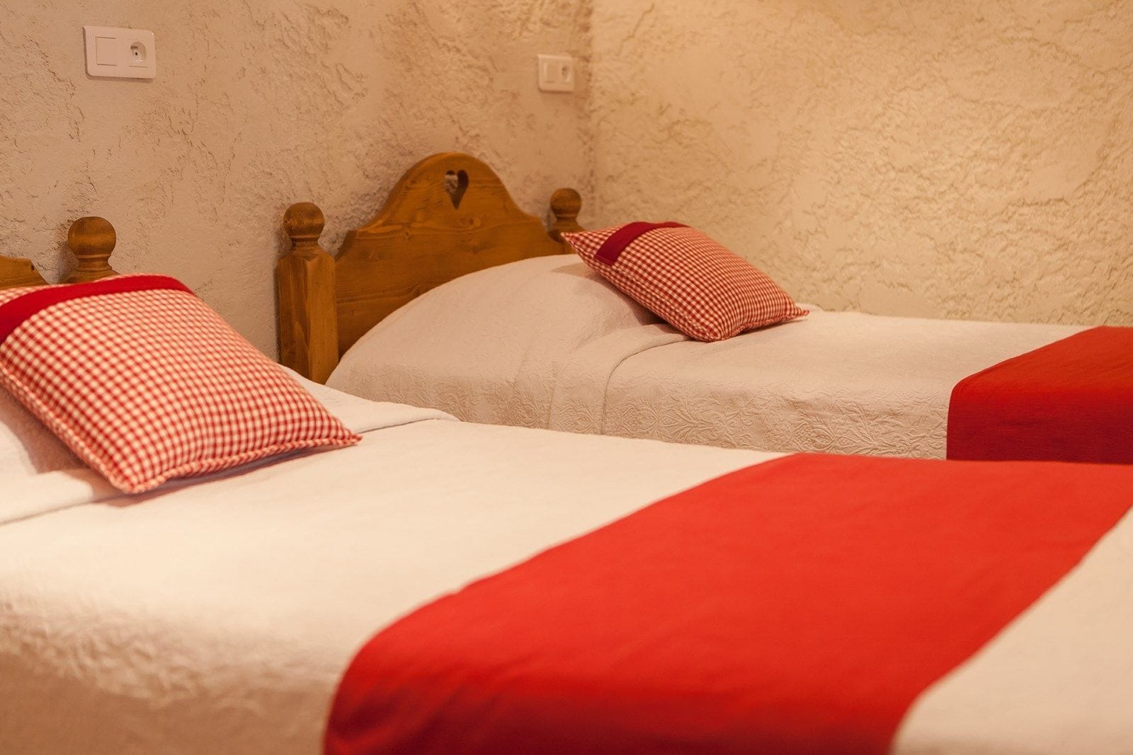 Deux lits simples avec des têtes de lit en bois, du linge de lit blanc et des touches de couleur rouge.