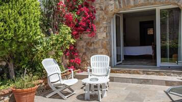 Une terrasse avec deux chaises blanches et une table, un mur en pierre et un pot de fleurs.