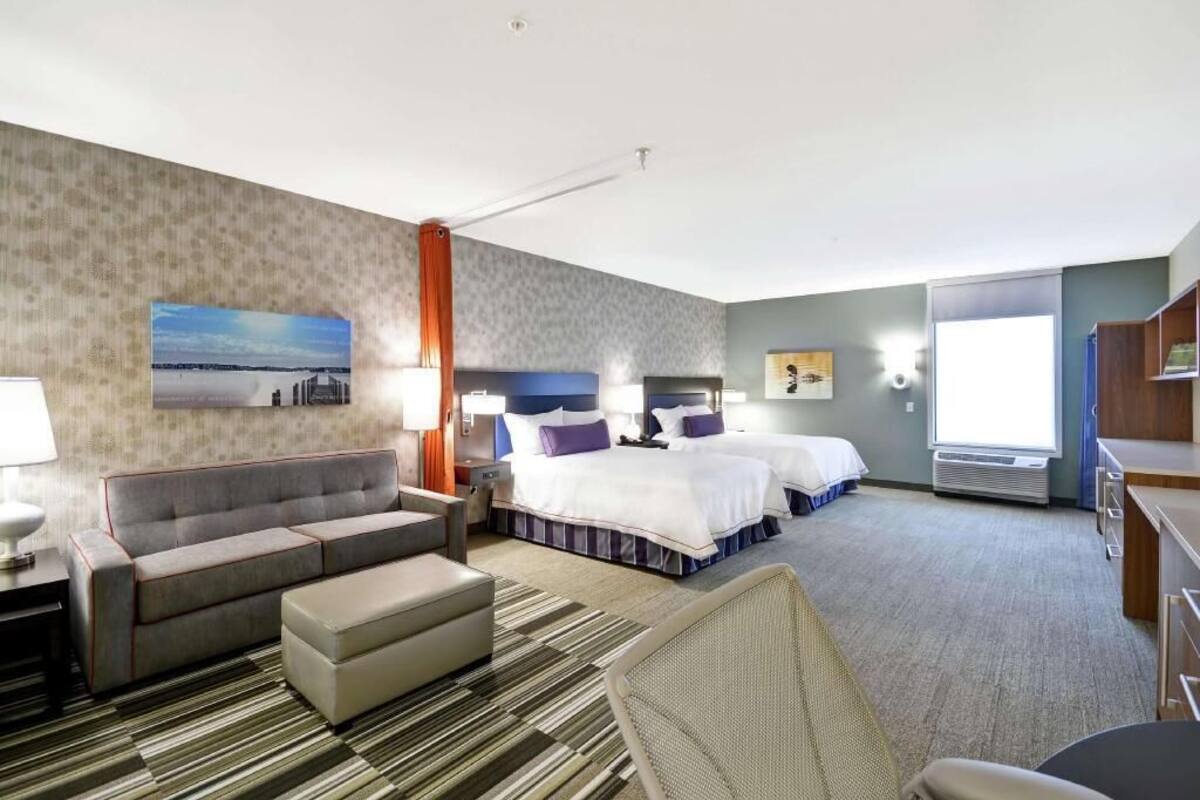 Une chambre d’hôtel avec un canapé, deux lits, un bureau, une chaise, une lampe et un tableau au mur.