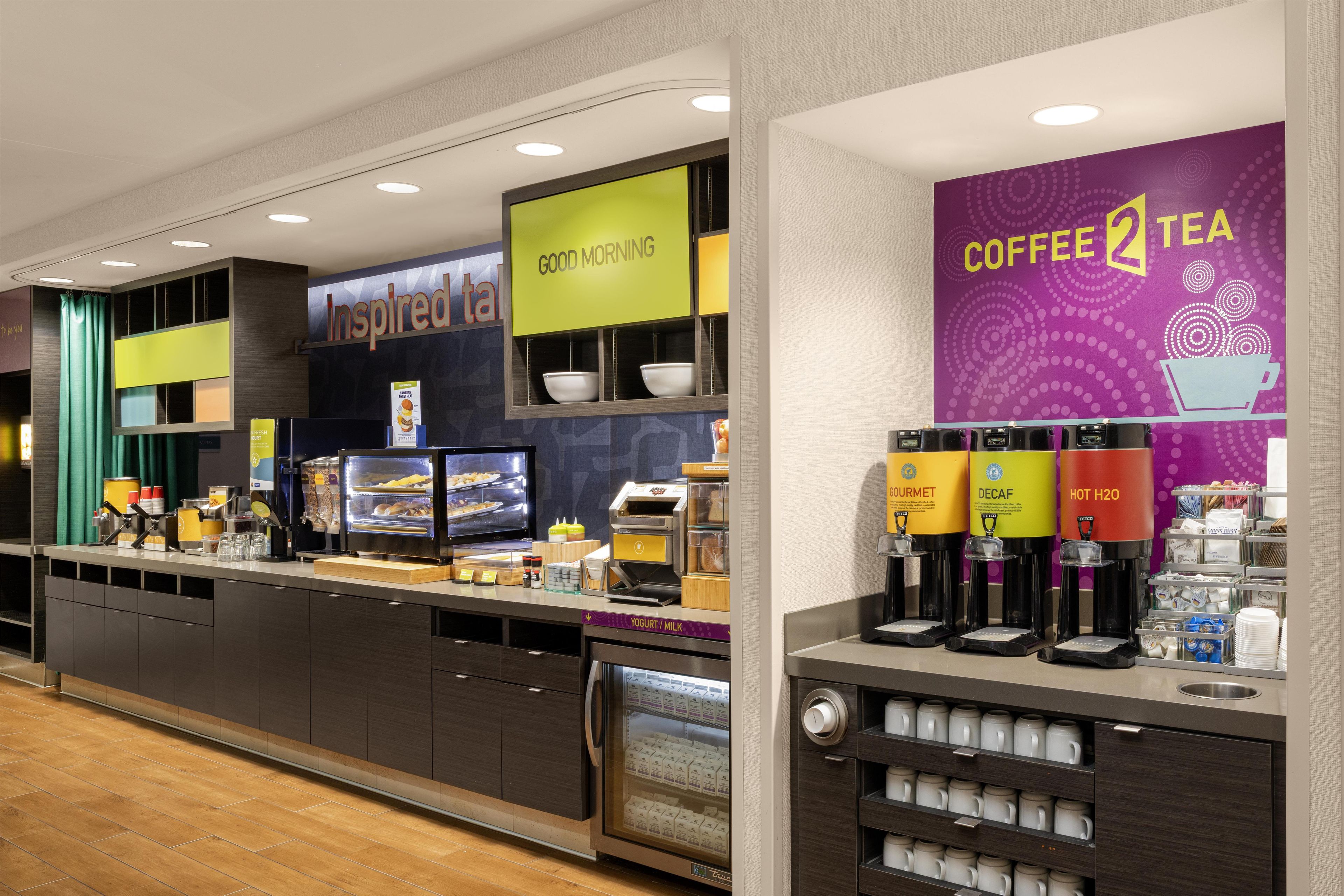 A modern coffee shop with a counter displaying various food items and a coffee station with multiple drink dispensers.