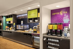 Ein modernes Café mit einer Theke, die verschiedene Speisen anbietet, und einer Kaffeestation mit mehreren Getränkespendern.