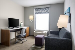 Habitación de hotel con escritorio, silla, computadora, lámpara, sofá y ventana con vistas.