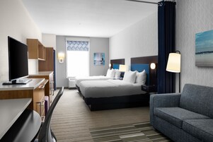 Habitación de hotel con cama, escritorio con computadora, silla, sofá y televisor.
