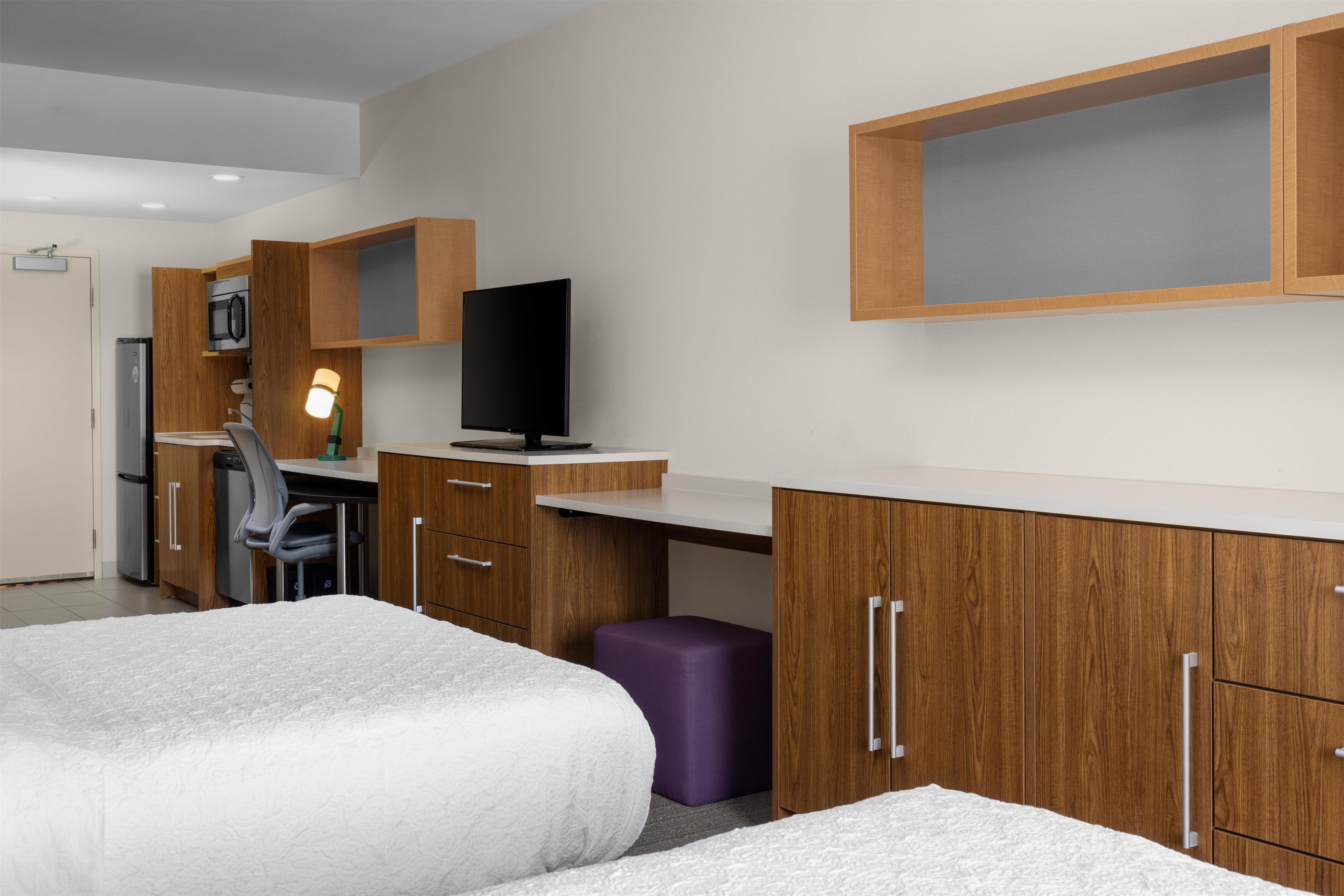 Una habitación de hotel moderna con cama, escritorio, silla, televisor y armario.