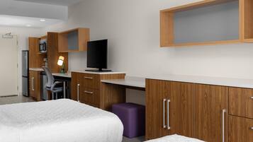 Una habitación de hotel moderna con cama, escritorio, silla, televisor y armario.