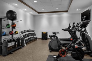 Une salle de sport équipée de matériel d’exercice, notamment un tapis de course, un vélo d’appartement et des supports pour les poids.