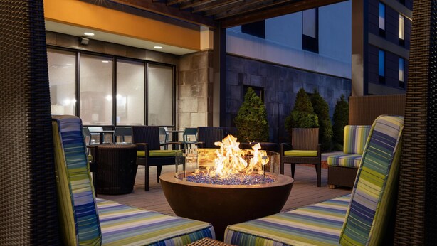 An outdoor seating area with wicker furniture and a central fire feature. - Home2 Suites by Hilton Minneapolis-Eden Prairie (Minnetonka)