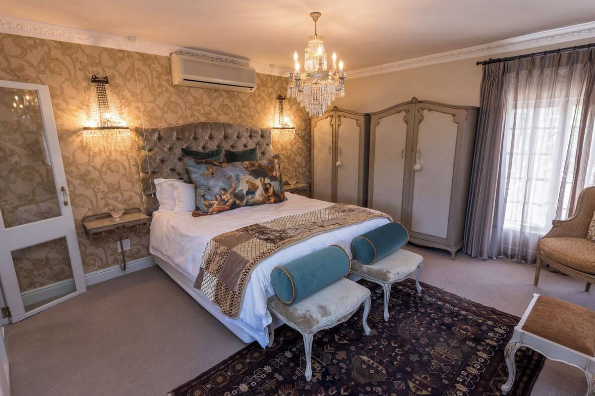 Une chambre à coucher avec un grand lit, un lustre, une armoire et un banc.