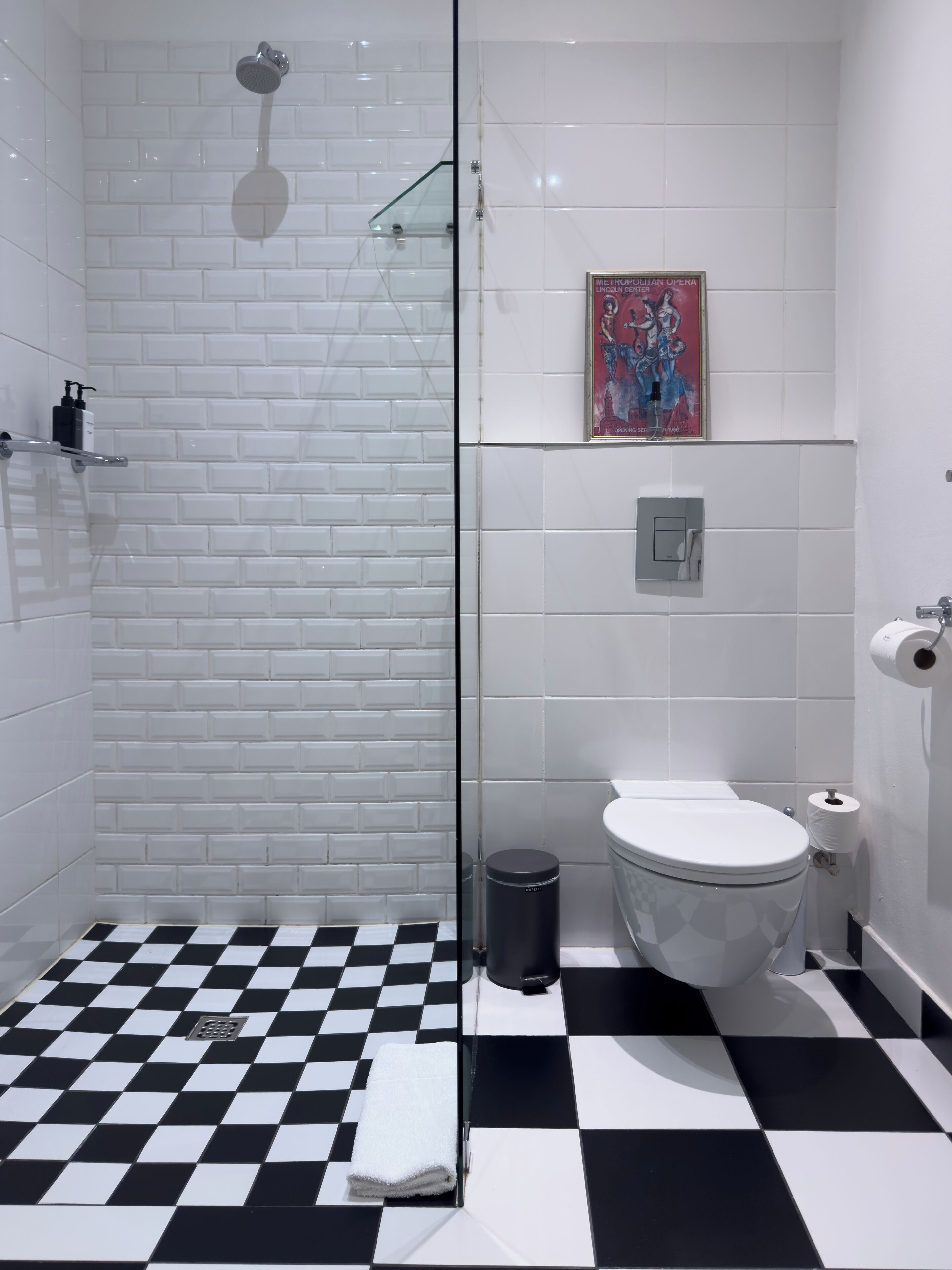 A bathroom with a checkered floor, a glass shower enclosure, a toilet, and a sink.