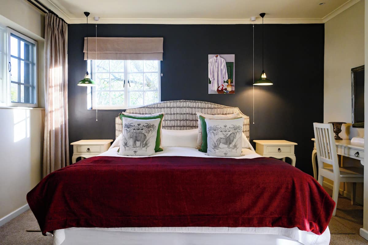 Une chambre avec un grand lit, deux tables de chevet, une chaise, un bureau, une fenêtre avec des rideaux et une lampe fixée au mur.