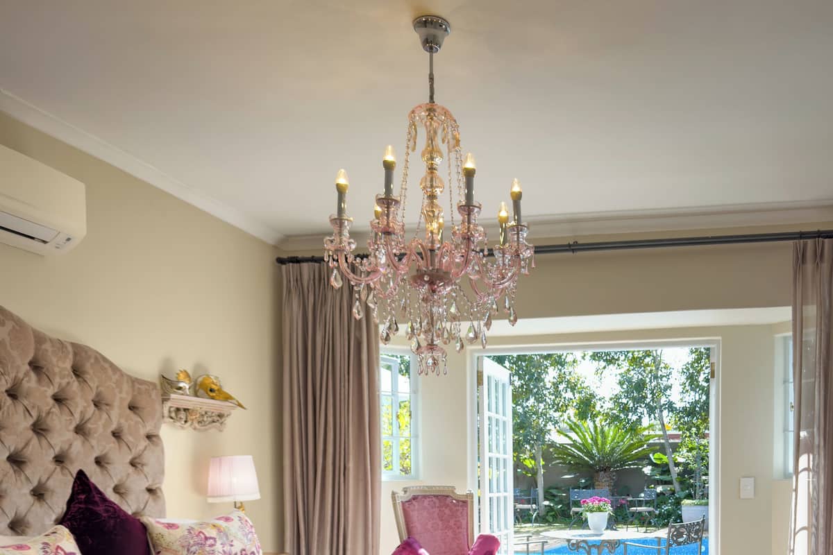 Une chambre avec un grand lit, un lustre, une vue sur la piscine et un balcon.
