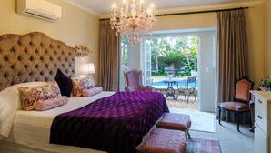 Een slaapkamer met een groot bed, een kroonluchter en uitzicht op een buitenzwembad.