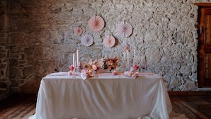 A table set with candles, flowers, and paper fans against a stone wall. - Paternoster Hotel (Paternoster)