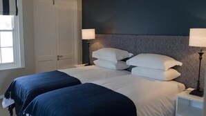 Een slaapkamer met twee bedden, witte beddengoed, een donker hoofdbord en nachtlampjes.