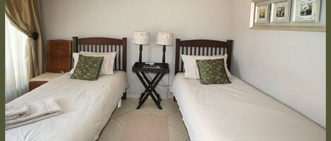A twin room with two beds, a small table with lamps, and a wall-mounted picture frame.