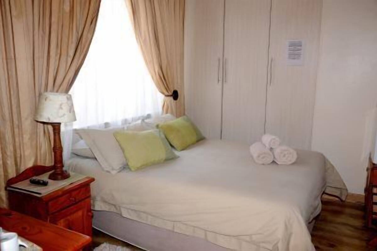 A bedroom with a bed, a nightstand, a lamp, and a window with curtains.
