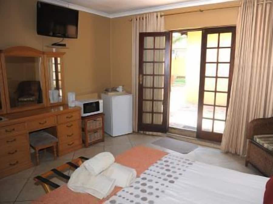 Ein Hotelzimmer mit Bett, Schreibtisch mit Stuhl, Fernseher, kleinem Kühlschrank und einer Schiebetür zum Außenbereich.