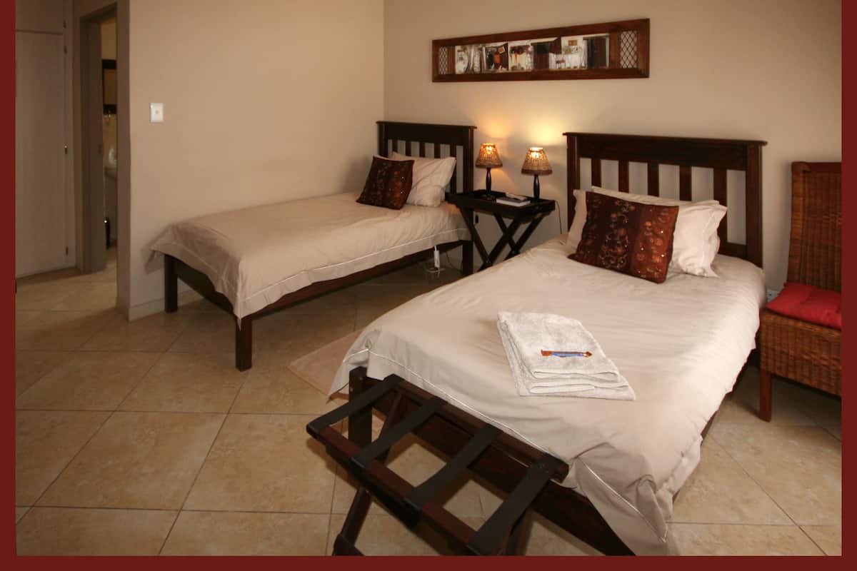 A hotel room with two beds, a wooden headboard, a small table with a lamp, and a chair.