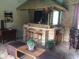 Una zona de bar con mostrador de ladrillo, taburetes de madera y techo de paja.