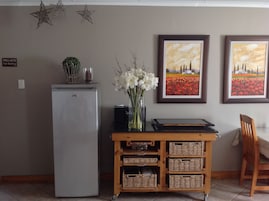 Un comedor con refrigerador, un carrito auxiliar de madera con cestas y dos cuadros enmarcados en la pared.