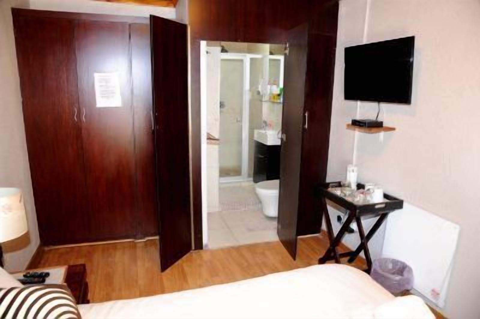 Une chambre d’hôtel avec une armoire en bois, un téléviseur fixé au mur, un bureau avec une chaise et une salle de bain visible à travers une porte ouverte.