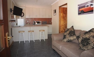 Un espacio habitable compacto con kitchenette, un sofá con cojines de estampado de leopardo y un televisor montado en la pared.