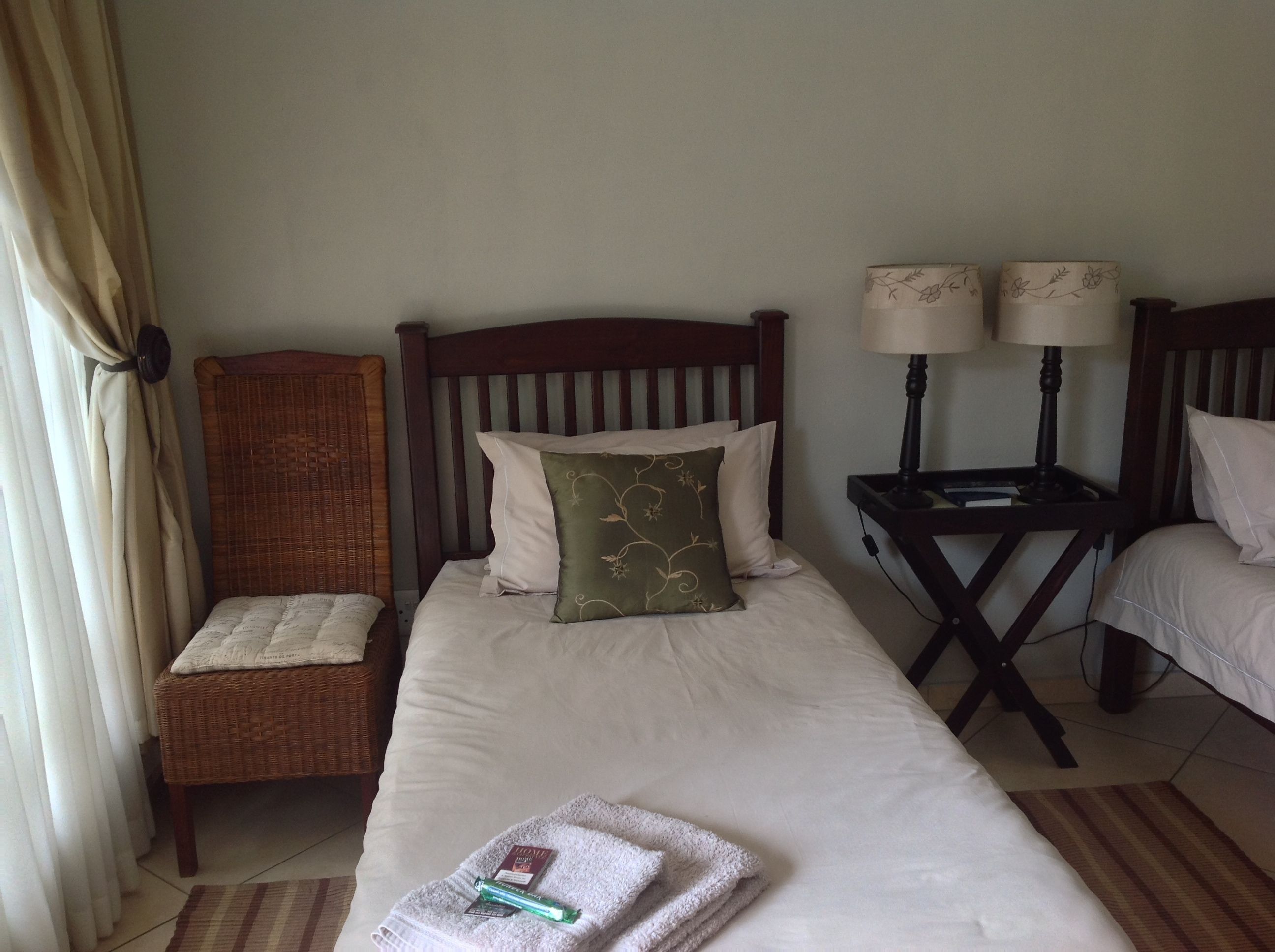 A hotel room with a single bed, a chair, two bedside lamps, and a small table.