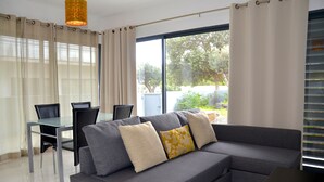 A modern living room with a grey sectional sofa, a glass dining table, and a large window with curtains. - VILAS ESPÍRITO SANTO by brugrani (Porto Santo)